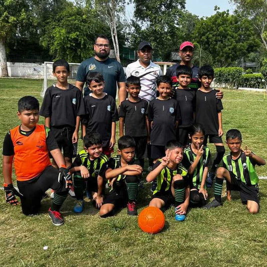 Group of children in sports uniforms with a coach on a grassy field.