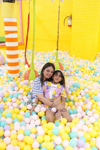 Woman and child in a ball pit with colorful balls and a yellow wall.