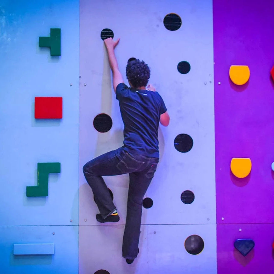 Person climbing a colorful wall in an indoor trampoline park