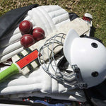 Cricket bat, ball, pads, helmets laid out on grass